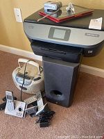 Photo showing HP Envy Photo 7155 printer atop Yamaha speaker with other electronics around, including tablet, cordless phones, and boombox