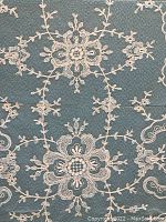 Close-up detail of antique ivory lace with floral and scroll patterns on fabric background.