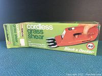 Photo showing the original Black & Decker branded box featuring the cordless grass shear and product info.
