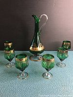Full set photo of green decorative wine decanter with six matching glasses on blue textured surface.
