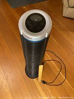 Full view of the black and silver TheraPure tower air purifier with a power cord and a ruler for size reference on wooden floor.