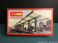 Front view of original box with illustrated lid showing large train station scene with platforms and passengers
