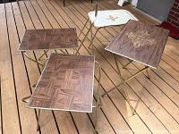 Four TV tables with woodgrain tops, two with gold decorative designs and two with parquet patterns, shown on folding gold metal legs.