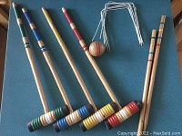 Four wooden croquet mallets, balls, and stakes arranged on a blue surface showing colors and condition.