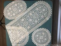 Vintage white lace doilies including a rectangular runner, round and oval doilies arranged on a blue background