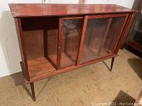 Full front view of wooden vintage sideboard showing glass sliding doors and legs.