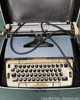 Top-down view of the typewriter showing the keyboard and paper holder with attached power cord.