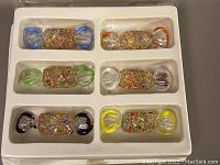 View of the 6 Murano glass candies arranged in molded tray, displaying different colored ends and speckled centers.
