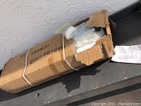 Damaged cardboard box labeled 3x9 meters with bundled contents inside, protecting white metal parts and fabric components for a canopy tent.