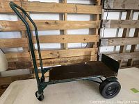 Full side view of green metal frame hand cart dolly with wooden base platform and handle, showing structure and size.