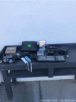 Full lot showing gaming consoles, controllers, remotes, and game discs arranged on table outdoors