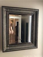 Front view of square wall mirror showing intricate carved frame and reflective surface.