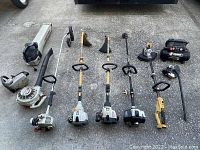 Photo showing a lineup of various small motor tools including weed walkers, a blower, a small chainsaw, and an air compressor on a concrete surface.