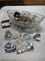 Photo showing leaded crystal bowl filled with assorted jewelry and several bags of costume jewelry and small jewelry box containing earrings.