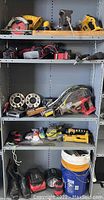 Shelf showing assorted tools including Dewalt circular saw, battery chargers, tennis and racquetball rackets, aluminum wheel spacers, buckets, paint roller handles, and various power tools.