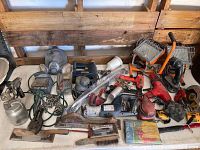 Overview of lot showing various power tools, hand tools, sprayers, and safety mask laid out on floor with wooden pallet background.
