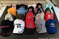 Full display of all 20 assorted baseball caps showing varied colors, logos, and designs on a black cloth surface