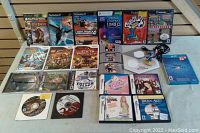 Photo showing a variety of video game titles including Wii, PS2, DS games, and loose discs and cartridges on a wooden surface.
