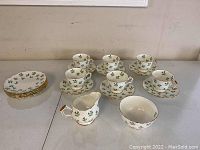 Full view of the set on table including 6 tea cups with saucers, stacked dessert plates, creamer, and sugar bowl