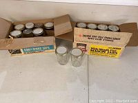 Boxed wide mouth Mason jars with metal and white lids, some jars loose in front of boxes.