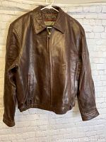 Front view of the brown leather jacket hanging on a hanger against a wall.