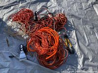 Photo showing multiple coiled extension cords in orange and other colors on tarp with bolt cutters at side