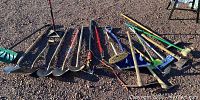 Photo showing the full set of landscaping and yard tools including shovels, tamper, pickaxes and brooms laid out on gravel.