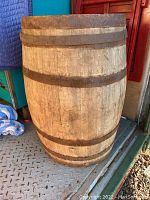 Front exterior view of large wooden barrel showing rusted metal bands and light wood staves.