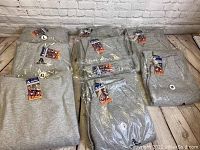 Gray men's sweatshirts and sweatpants laid out on a floor, all tagged new by Akadema Sportswear.