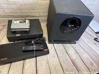 Lot includes MTS HTS-3200 subwoofer speaker, LG Blu-ray player with remote, JVC KS-S31 car stereo head unit, and RCA VCR all placed on the floor.