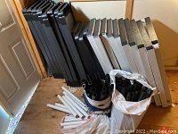 Black and white plastic shelving panels stacked vertically against wall with black and white plastic tubes stored nearby in buckets and bags.