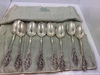 Eight Florentine Lace spoons arranged in a cloth roll pouch