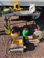 Overview of multiple tools laid out on folding table including saws, leaf blower, sprayers, and tile cutter.