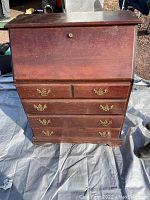 Front view of wooden secretary desk closed showing four drawers with brass pulls, some pulls missing, and drop-front panel with lock keyhole.