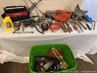 Wide view of assorted automotive and general hand tools displayed on a white cloth. Includes HUSKY tool bag, power steering fluid, hand tools, orange extension cords, and green tub of hardware.