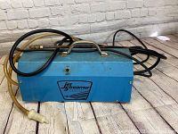 Blue metal case of the power washer with attached hoses and handle visible, placed on wooden floor.