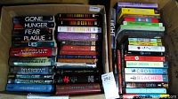 Two boxes of used young adult fiction books, showing a variety of titles and authors with worn conditions
