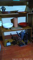 Shelf of mixed items including bowls, a watering can, and figurines displayed on a wooden shelving unit.