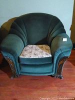 Front view of green upholstered armchair with floral seat cushion, scalloped back, and wooden carved armrests and legs.