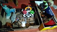 Full lot in two boxes showing assorted cultural and collectible items including marionette doll, Statue of Liberty, boomerangs, flatware and miniature drum.
