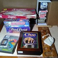Photo of various board games stacked, including Scrabble box, Mastermind, Trivial Pursuit, Clue in wooden box, and multiple card decks