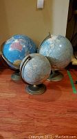 Three vintage globes grouped together on a hardwood floor
