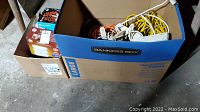 Cardboard box labeled Banker’s Box containing assorted extension cords in multiple colors and boxes of light bulbs.