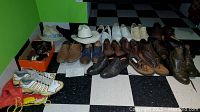 Multiple pairs of men's shoes mostly size 10 including brown, black, casual and dress shoes, white hats and shoe supplies on black and white checkered tile floor.
