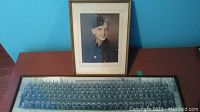 Two framed vintage military photos shown side by side, one is a large group photo in a black frame and the other a smaller portrait in a gold frame.