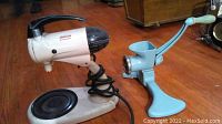 Front side view of Sunbeam Mixmaster stand mixer and light blue manual meat grinder on wooden floor surface.