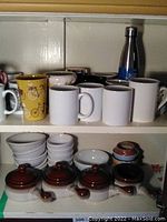 Two shelves of cups, mugs, bowls, and bean pots inside a cabinet
