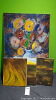 Four original paintings on canvas displayed against a green wall; largest painting depicts colorful abstract floral still life; three smaller paintings are abstract with tones of yellow, brown, and orange.