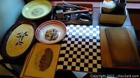 Photo showing assortment of kitchen items including wooden and ceramic platters, bowls with painted scenes, and metal utensils in container
