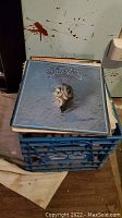 Milk crate filled with LPs, top album showing stylized band logo over a fish sculpture on ice